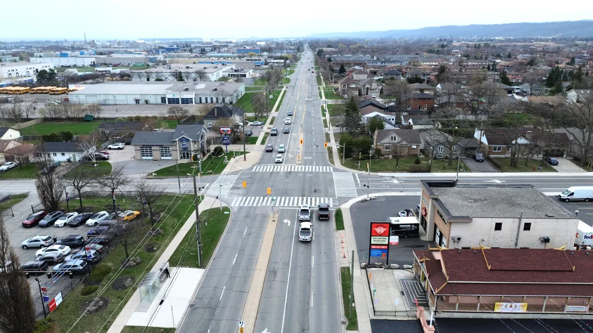 Aerial view along Barton Street East toward the Dewitt Road junction, a digital billboard across the intersection and the escarpment behind