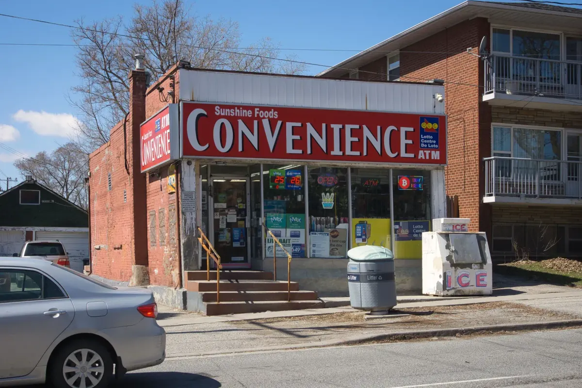 An independent convenience store in Toronto with a red Convenience sign and an ice freezer by the door