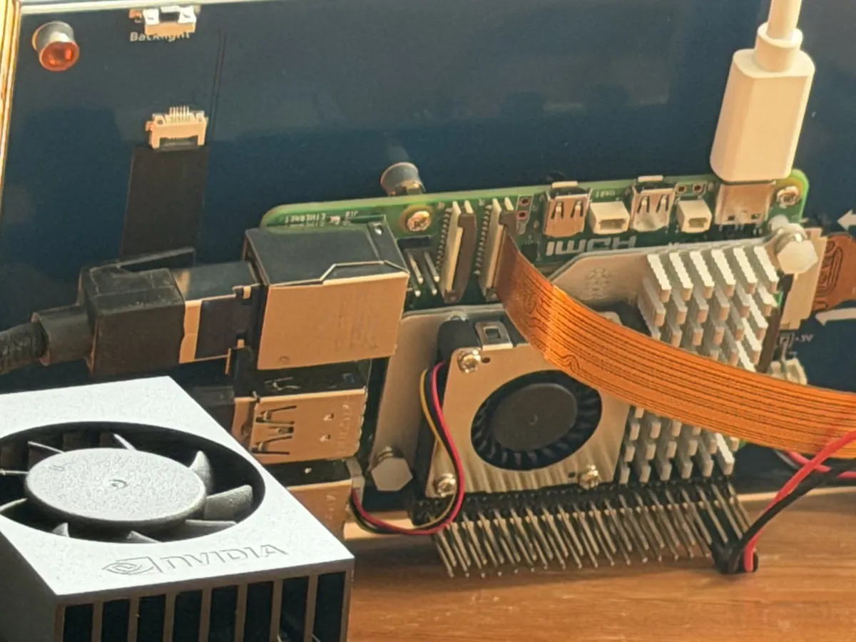 A Raspberry Pi 5 and an NVIDIA Jetson heatsink on a workbench, joined by an orange ribbon cable