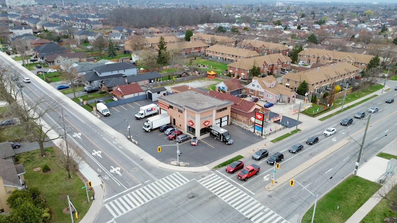 Oblique aerial of the corner property showing a queue of cars at the signal and dense residential streets beyond