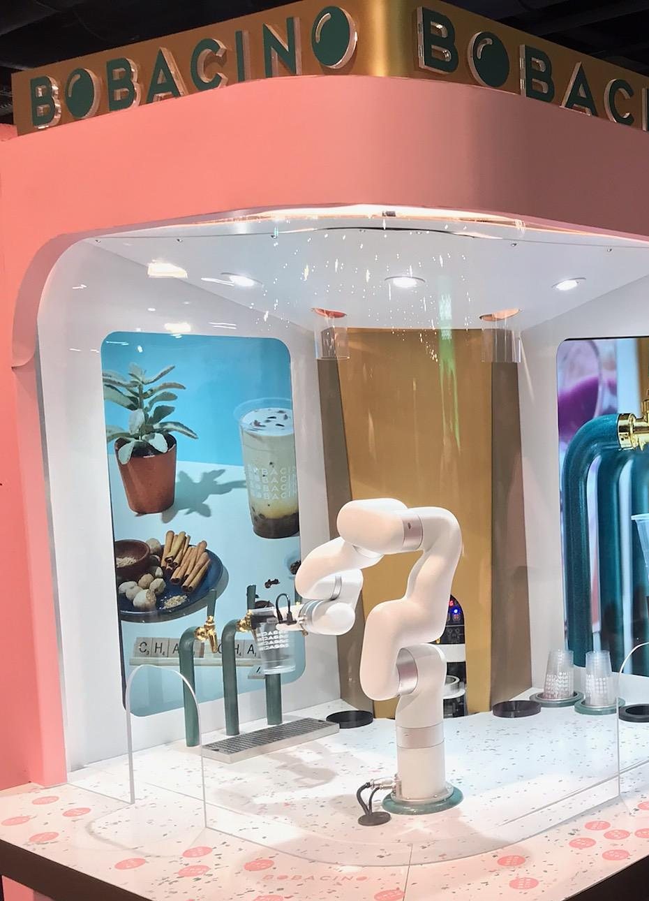 Bobacino’s pink demonstration bar with gold lettering, a white robot arm inside its lit glass bay beside gold taps