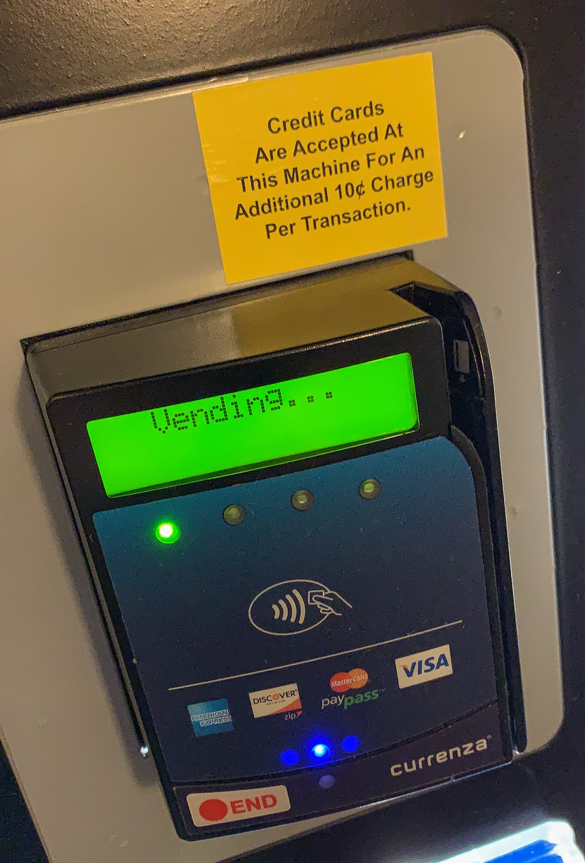 A retrofitted card reader on a vending machine, its display reading Vending, under a sticker about a ten-cent card charge