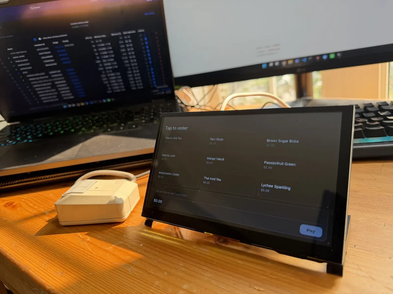 The bench kiosk, a small touchscreen on a wooden bench, showing a tap-to-order drink menu