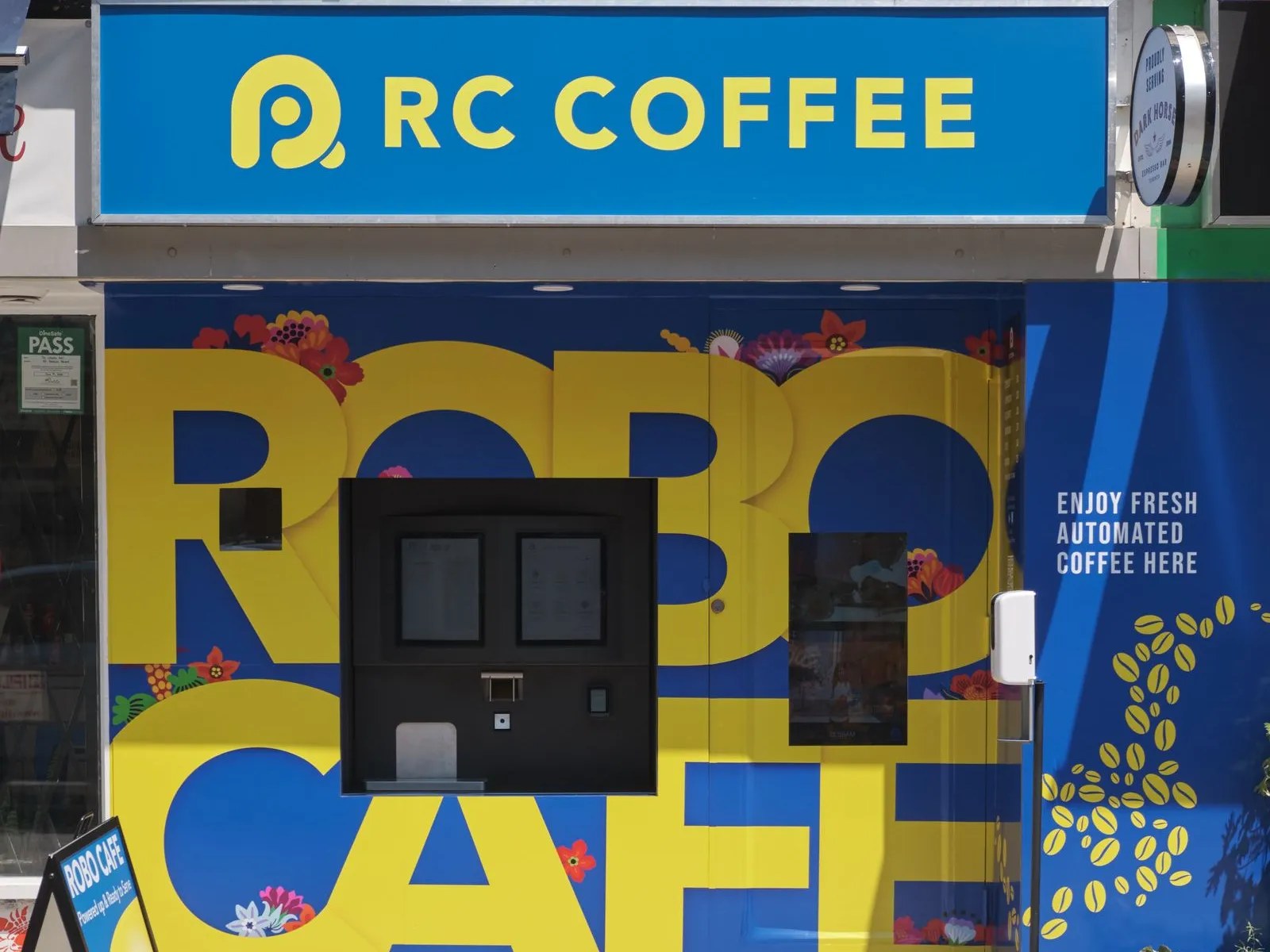 RC Coffee Robo Cafe storefront on a Toronto sidewalk, an automated espresso kiosk set into a blue and yellow wall