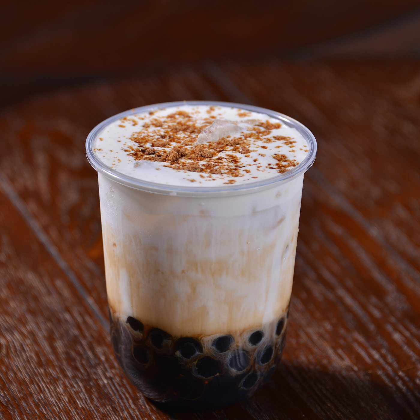 A cup of milk tea with dark tapioca pearls settled at the bottom, on a wooden table