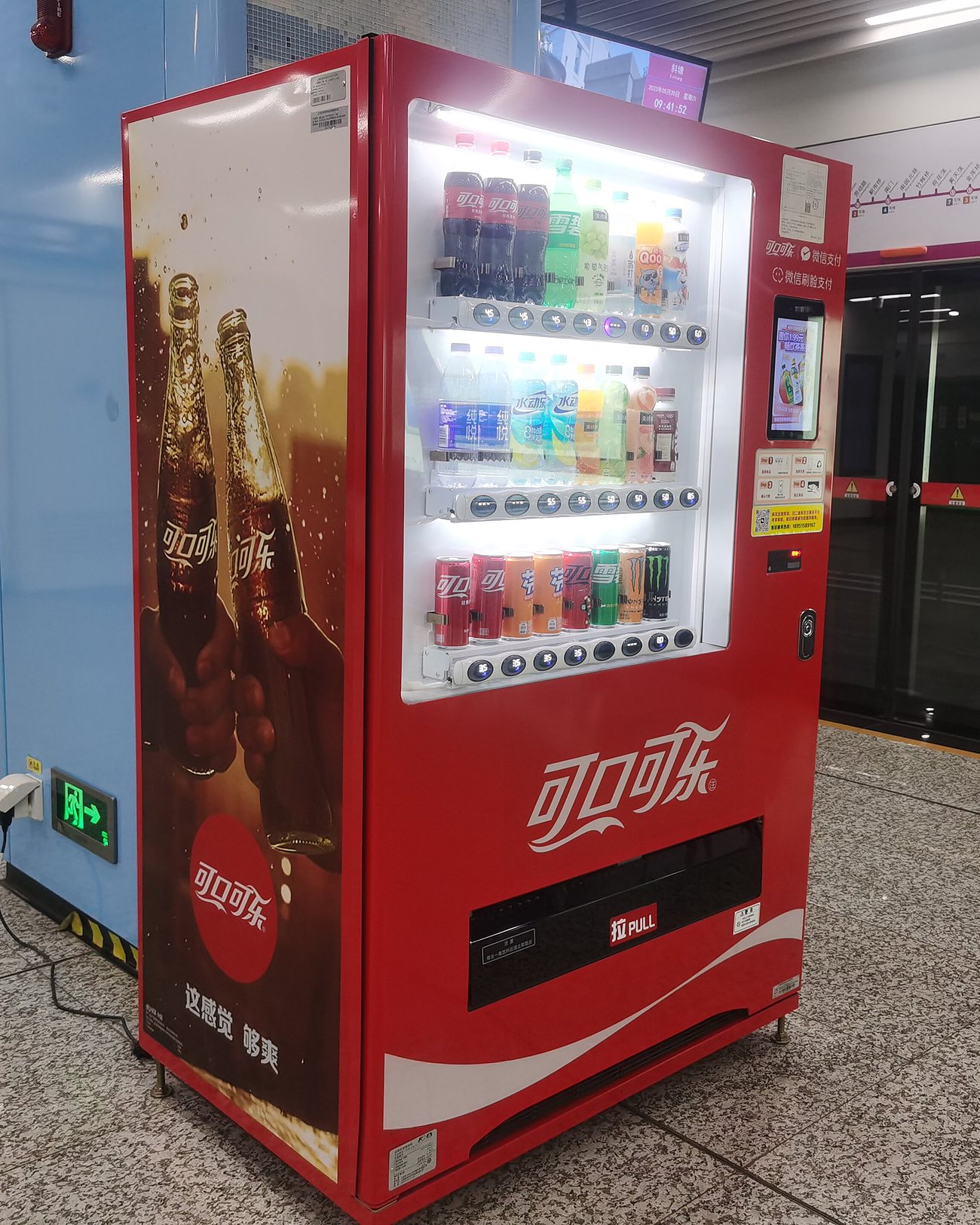 A red Coca-Cola vending machine on a metro platform in Suzhou, a payment panel built into its side
