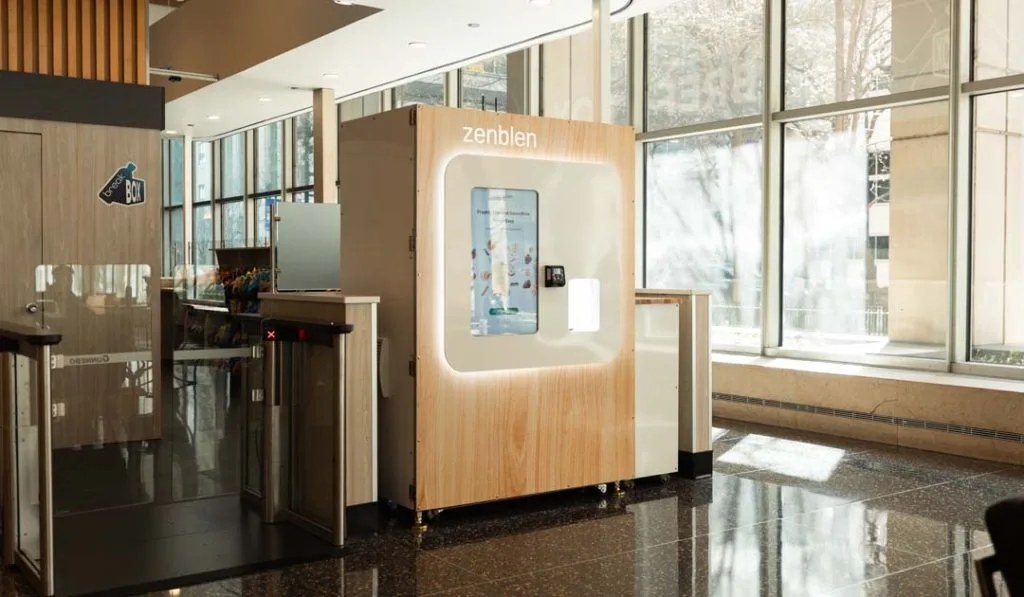 Zenblen robotic smoothie kiosk in a glass-walled building lobby next to security turnstiles